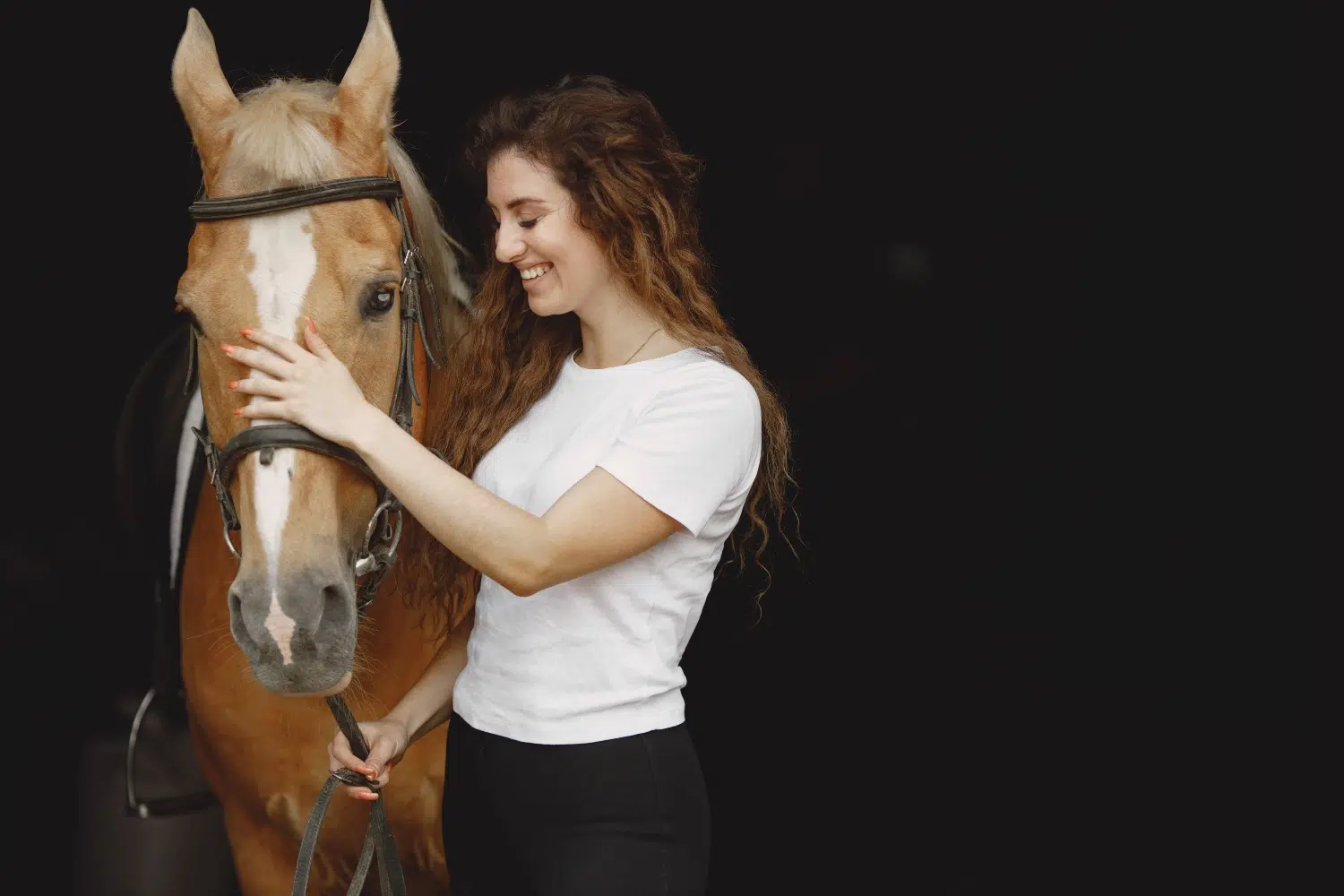 Cavalière à côté de son cheval en train de lui parler sur un fond noir
