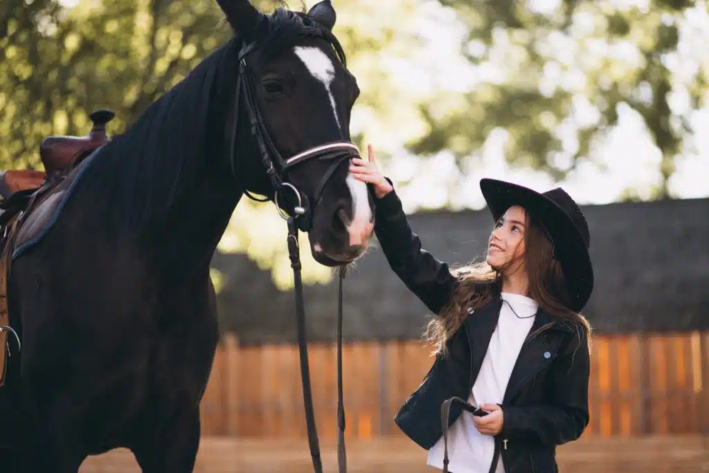 Jeune fille avec un chapeau de cow-boy qui caresse le nez d'un cheval noir