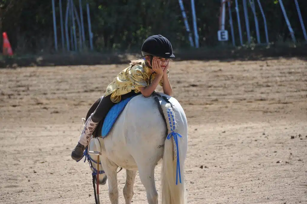 Fillette coiffée d'une bombe et allongée sur son cheval en train de faire la moue
